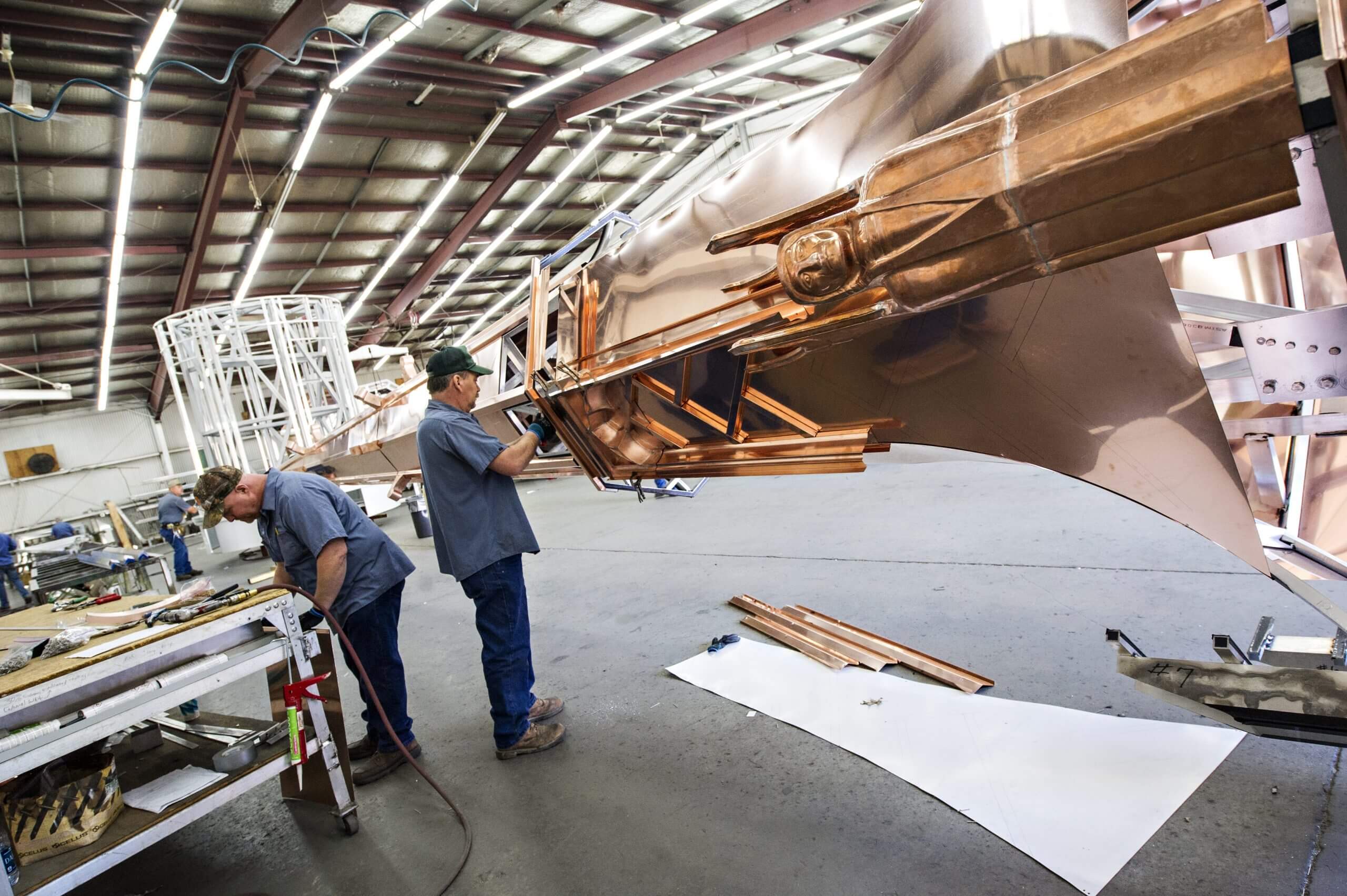 Two men constructing the copper steeple with copper angels