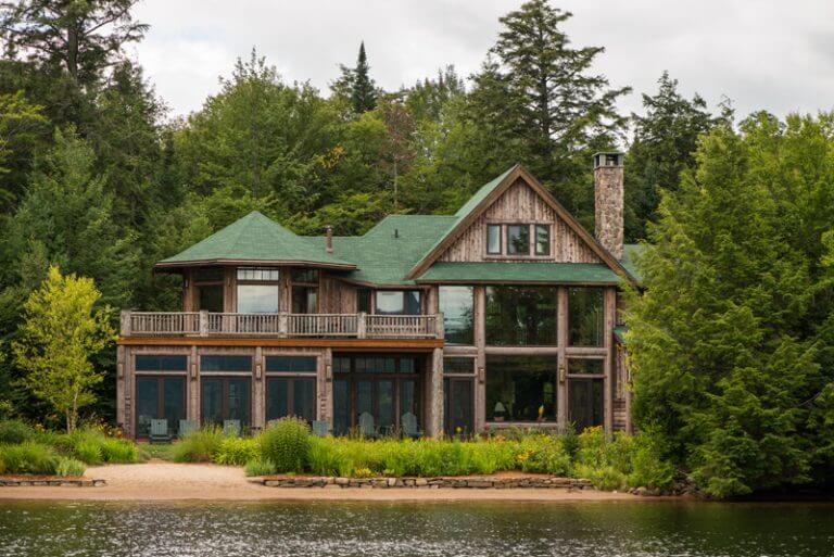 wood sided lake house with large windows and sand beach