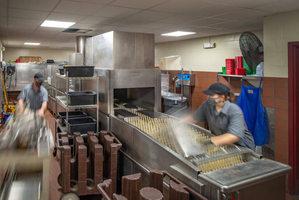 Food Service staff load and unload a large commercial dishwasher in the Frank Dining Hall kitchen